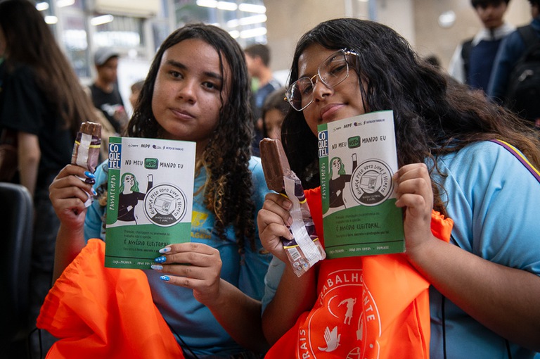 2026 1020 Entrega cartilha voto-8.jpg Jovens estudantes recebem cartilha "No Meu Voto Mando Eu" em ação de conscientização sobre a importância das eleições dentro do Programa Justiça e Cidadania