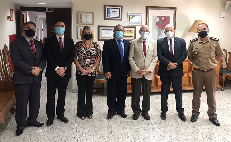 Foto de seis homens e um mulher. Eles estão em pé, lado a lado, em uma sala de piso e paredes brancas.