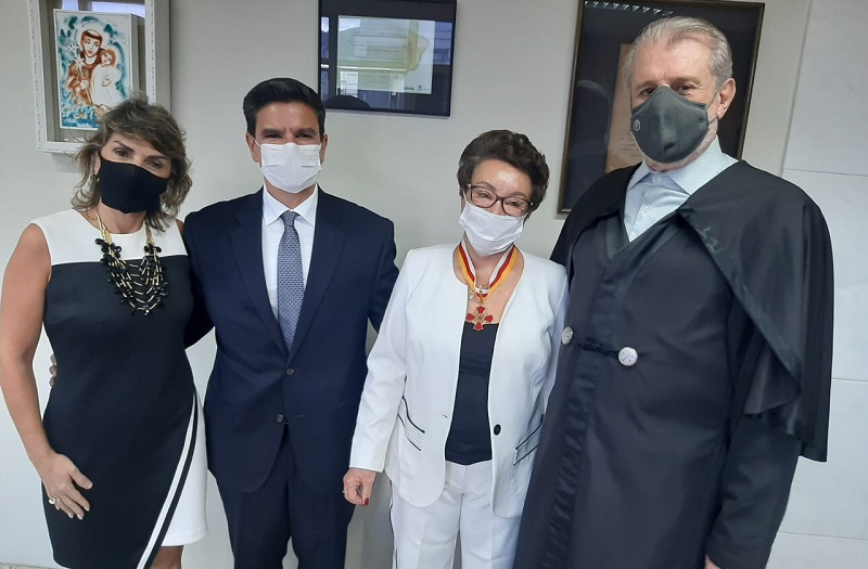 Foto da desembargadora Gisele Macedo Viera Dias; o juiz Bruno Alves Rodrigues, filho da homenageada; a advogada Maria Belisário; e o presidente do TRT-MG, desembargador José Murilo de Morais. Eles estão um ao lado do outro. A homenageada usa a medalha Ari Rocha, que acbaou de receber. Ao fundo, uma parece com dois quadros. 