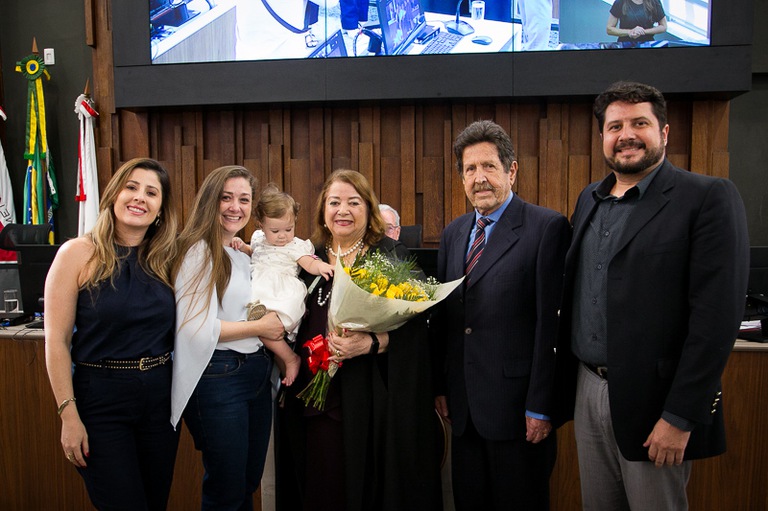 foto da desembargadora Maria Lúcia Cardoso de Magalhães com flores nas mãos ao lado de familiares