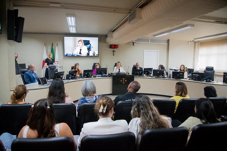 foto da mesa de honra com a presidente do TRT-MG, desembargadora Denise Horta, sentada ao meio falando ao microfone. A plateia aparece. 