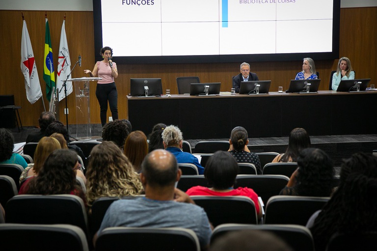 foto da servidora do TRT-MG Priscila La Gatta Carminate falando no microfone de frente para a plateia e ao lado da mesa de honra