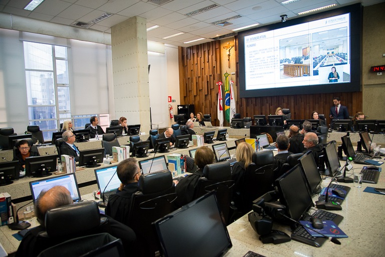 foto do plenário com a presidente do TRT-MG e telão ao fundo e os desembargadores sentados de toga preta