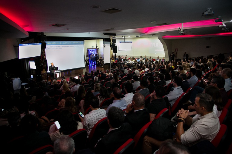 foto da plateia sentada e o presidente do TRT-MG no fundo em pé palestrando 