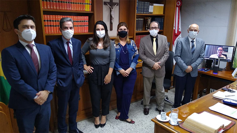 Foto das autoridades citadas no texro, uma ao lado da outra, Ao fundo está uma estante com livros e, à frente das autoridades está uma mesa de trabalho com papeis. Aa lado da ultima autoridade, hpa um computador sobre uma mesa pequena. 