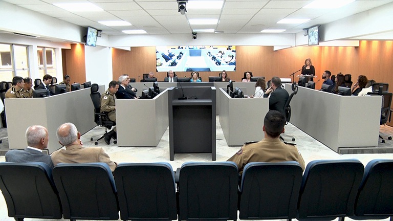 Foto do auditório mostrando os participantes assentados e três pessoas na plateia de costas