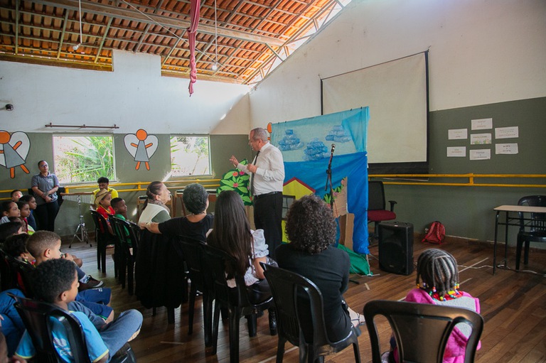foto do desembargador Marcelo Pertence sem paletó palestrando para crianças e adolescentes em frente de sala de aula do projeto Querubins