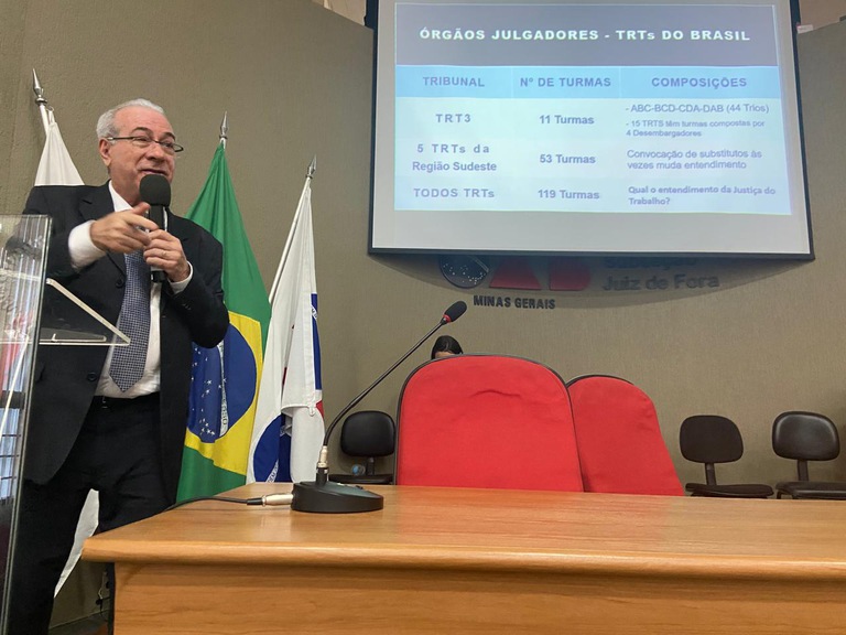 Desembargador Sebastião Geraldo em pé de terno palestrando 