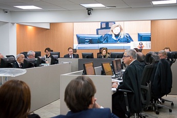 foto dos desembargadores sentados de toga preta durante o pleno com imagem da presidente do TRT-MG projetada no telão ao fundo