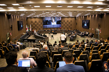 foto do plenário do evento cheio com a presidente do TRT-MG falando no telão