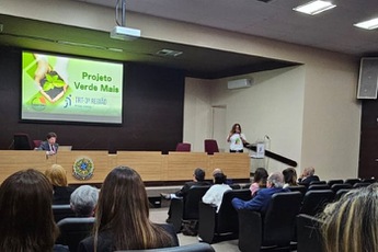 foto da servidora Júnia Paula Fernandes de Oliveira apresentando ações do TRT para plateia com telão no fundo
