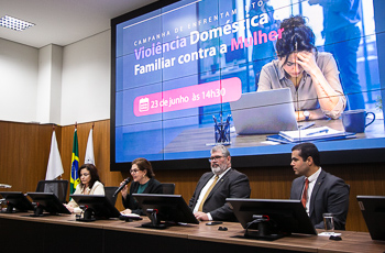 Foto da mesa de honra e telão ao fundo com arte do evento
