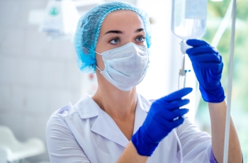 Foto de uma enfermeira verificando o soro. Ela está usando máscara facial e luvas de borracha.