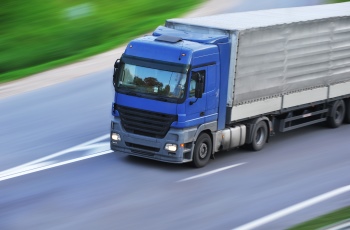 Foto de um caminhão truck azul trafegando pela rodovia.