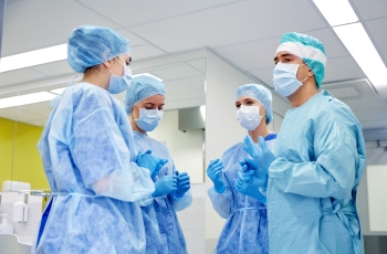 Foto de médicos preparados para iniciar uma cirurgia, aguardando para entrarem na sala de cirurgia.
