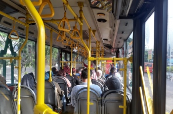 Imagem do interior de um ônibus, onde os passageiros estão sentados. Eles aparecem na foto de costas.