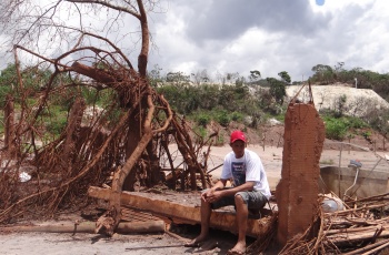 Após o rompimento da barragem de Fundão, em Mariana, um jovem usando um boné vermelho, sentado no meio dos escombros, observa, com uma expressão triste, o cenário de devastação deixado pela lama tóxica. Foto cedida pela Prefeitura Municipal de Mariana.