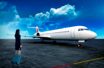 Imagem de uma mulher de costas segurando e puxando uma mala de rodinhas, preparando-se para entrar no avião, que está ao fundo, aguardando a acomodação dos passageiros.