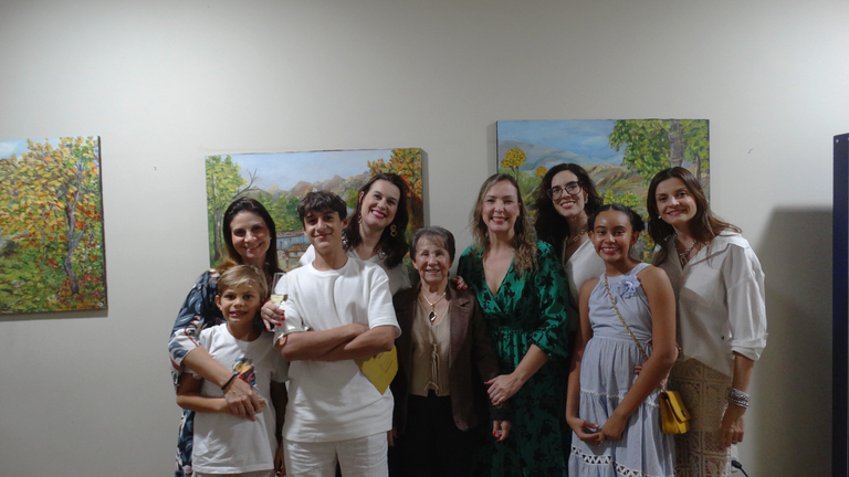 A imagem mostra a artista plástica Helena Oliveira reunida com seus familiares na abertura da exposição.