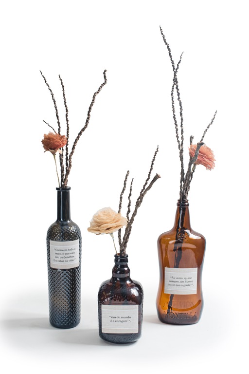 Figura 3 Sertão Sustentável.jpg Três garrafas de vidro âmbar com formatos diferentes usadas como vasos para flores e galhos secos