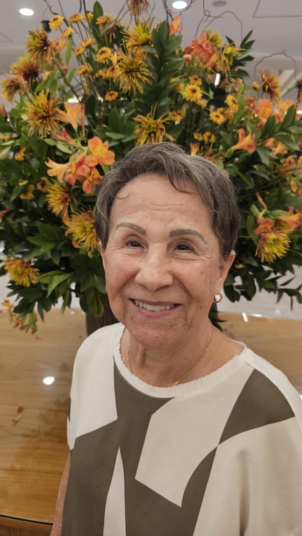 Foto da artista plástica Helena Oliveira em frente a um jarro de flores amarelas.