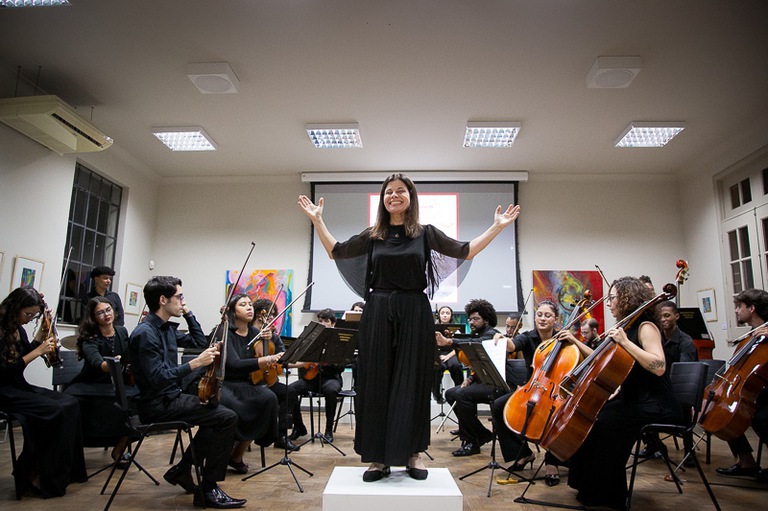 No centro da imagem a maestra Luciane Vilani, ao final de uma das músicas performadas, recebendo os aplausos do auditório. (Foto: SECOM)