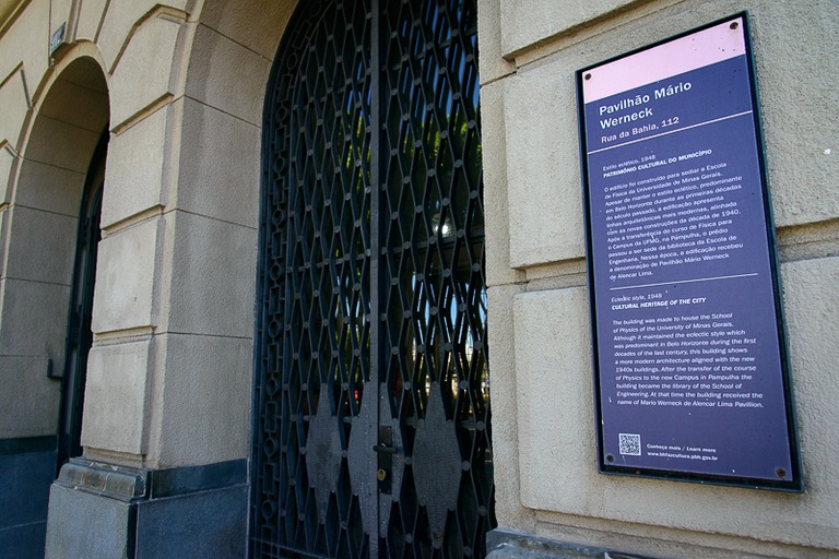 Foto da parte externa do prédio contendo uma placa de identificação