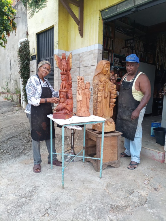 Eustáquio e Helena em pé apresentando três de suas obras para a foto