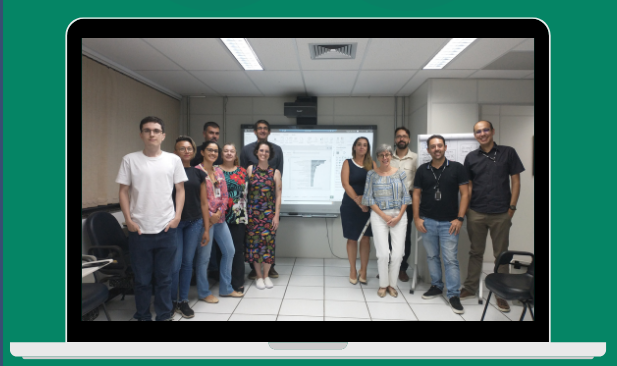 Doze participantes da oficina UaiCon em frente a uma imagem projetada do protótipo de painel criado durante a oficina