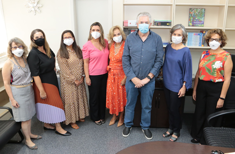 Foto dos participantes da reunião de pé, no gabinete da desembargadora Jaqueline Monteiro de Lima, todos de pé, à frente de uma estante branca, fazendo uso de máscaras faciais. 